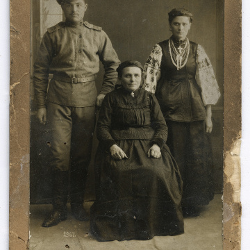 Man in World War I military uniform and two women in traditional attire