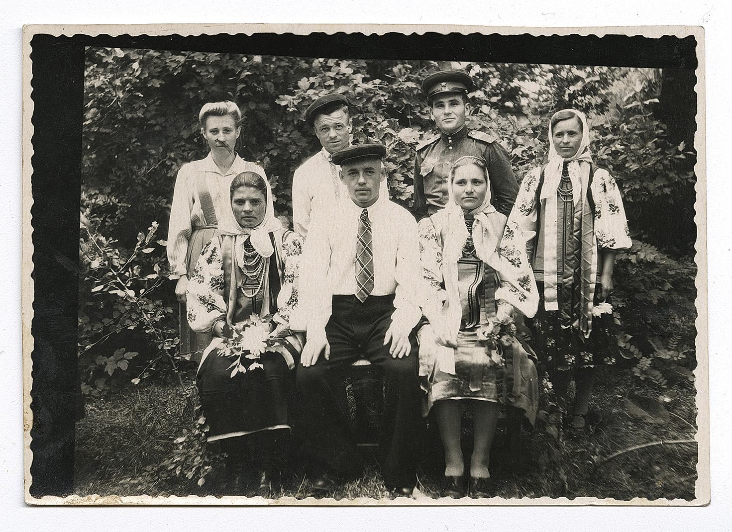 Троє чоловіків, один у вишитій сорочці, один у військовій формі, та чотири жінки, троє у народному вбранні