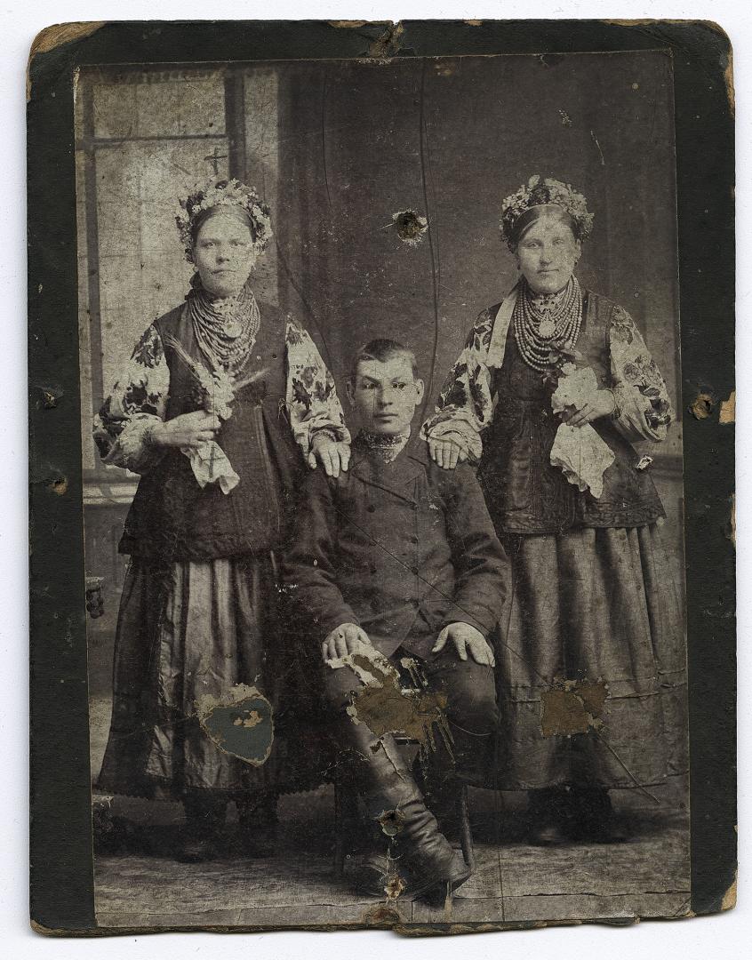 Хлопець у вишитій сорочці під верхнім одягом та дві дівчини у народному вбранні