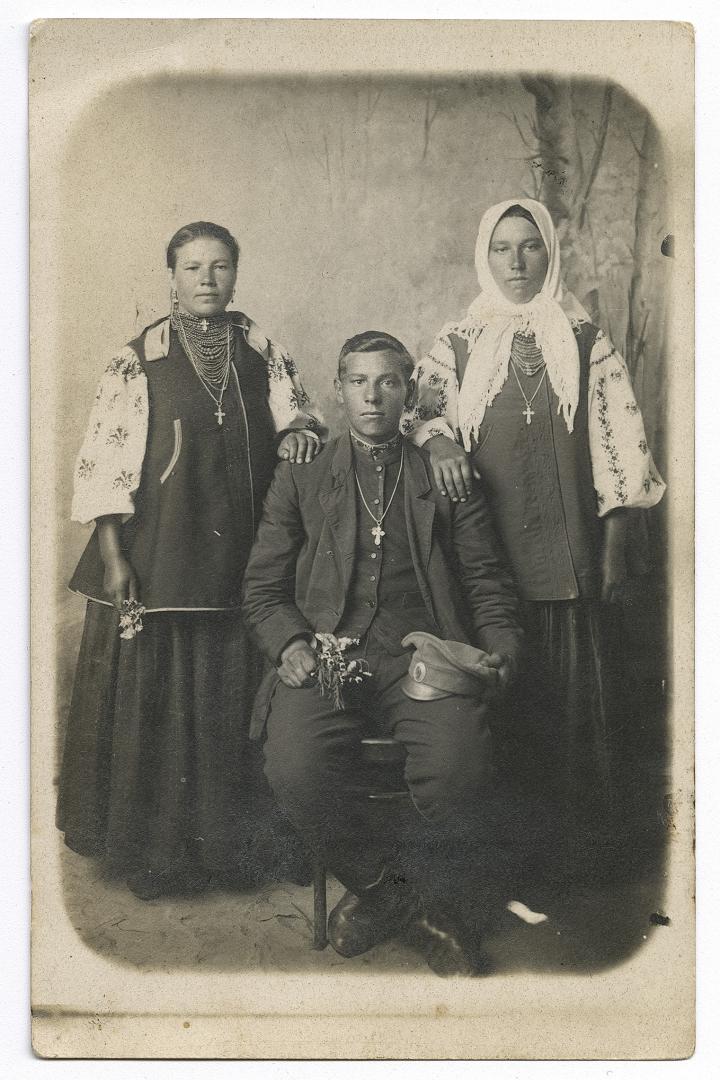 Woman and girl in traditional attire and a boy in an embroidered shirt under outerwear