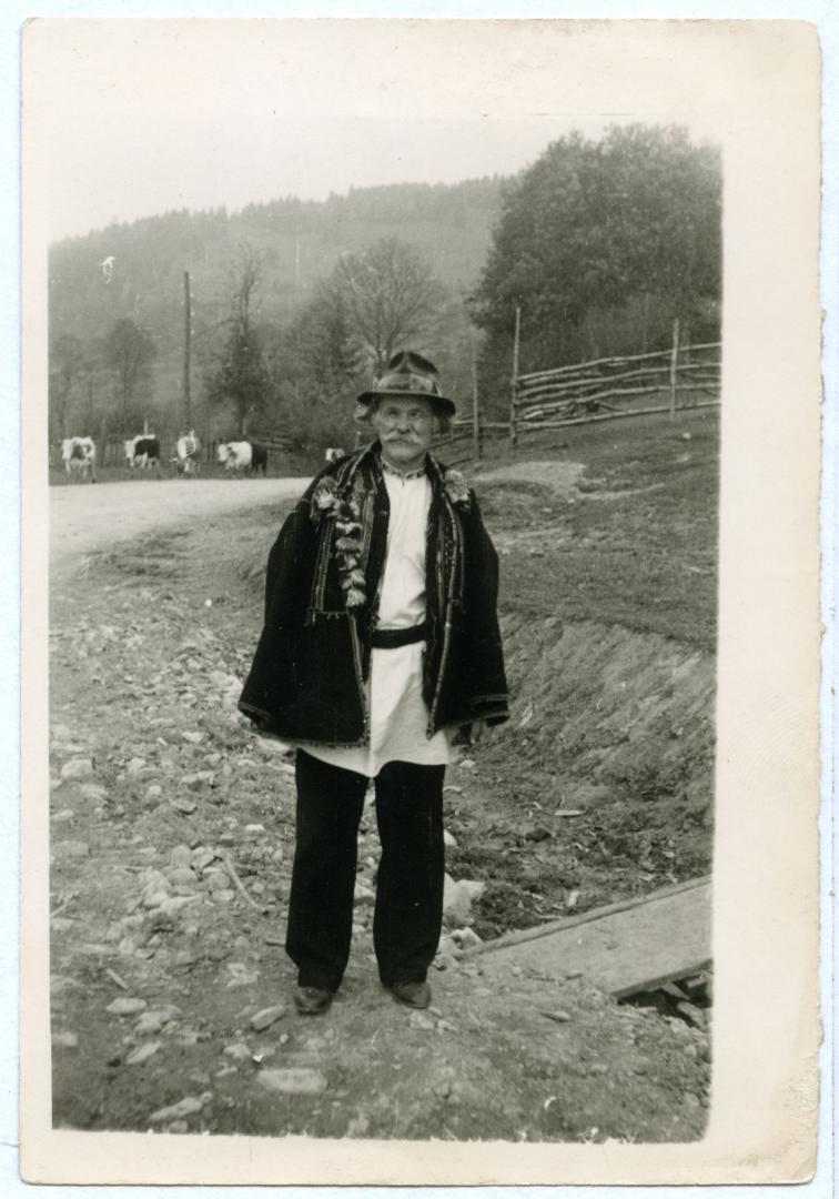 Photo. A man wearing a serdak (short over coat) and a kresania (handmade felt hat) in a village street