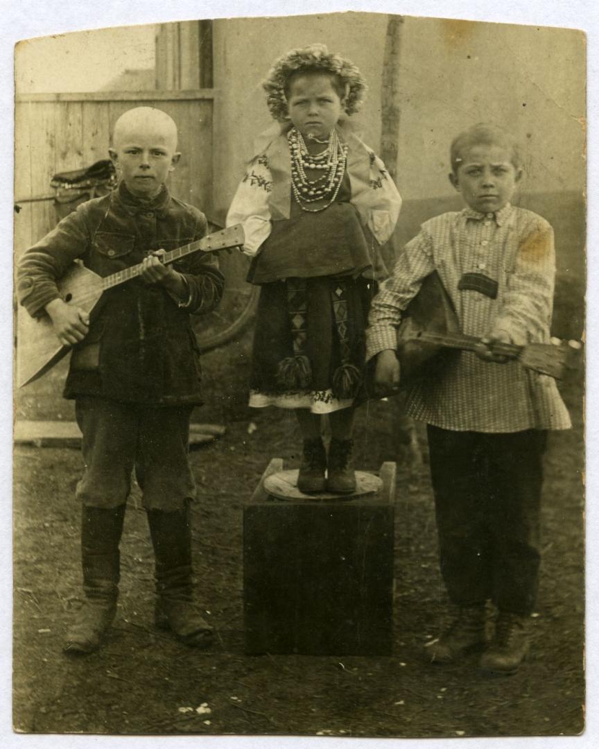 Photo. A girl and two boys holding balalaikas all wearing folk attire