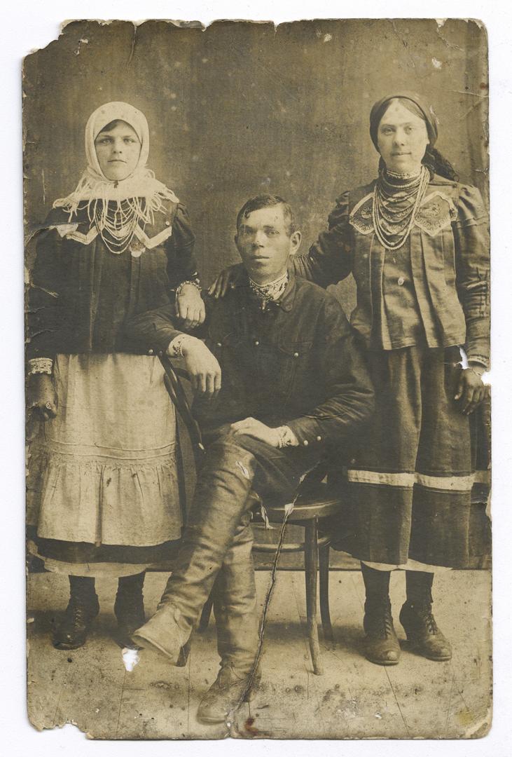 Family photo. Man in an embroidered shirt under outerwear and two women in traditional jewelry
