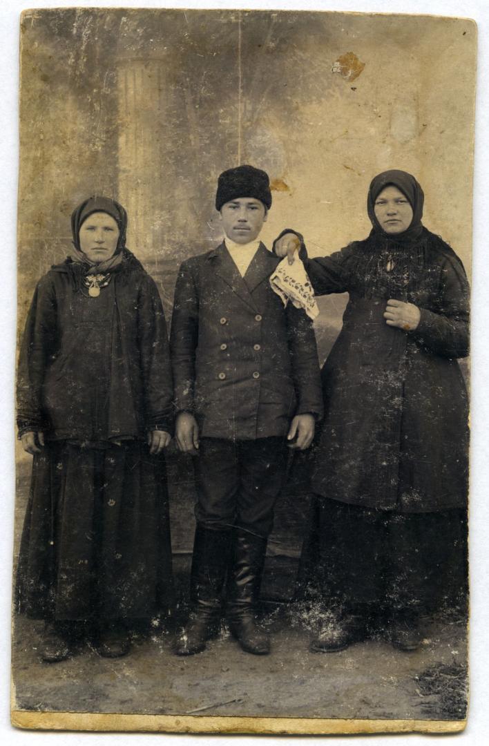 Photo. A man standing with two women wearing folk attire
