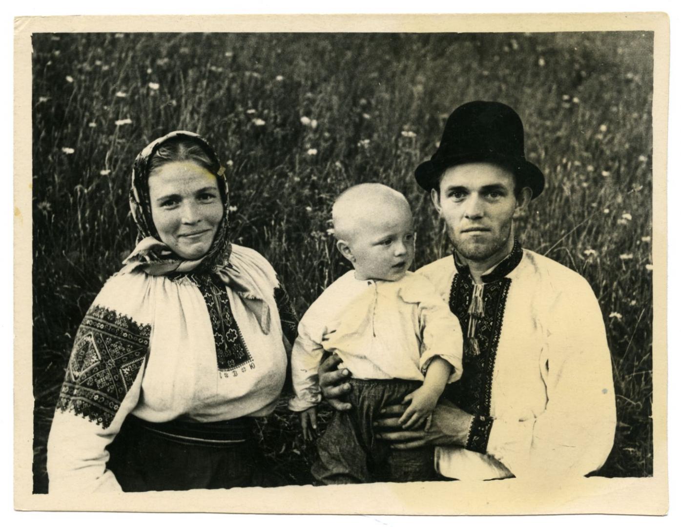 Photo. A woman and man holding a boy wearing folk attire