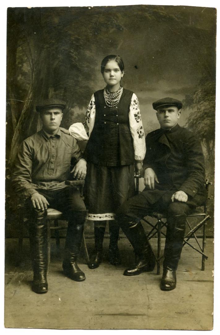 Photo. A girl wearing a folk attire with two men