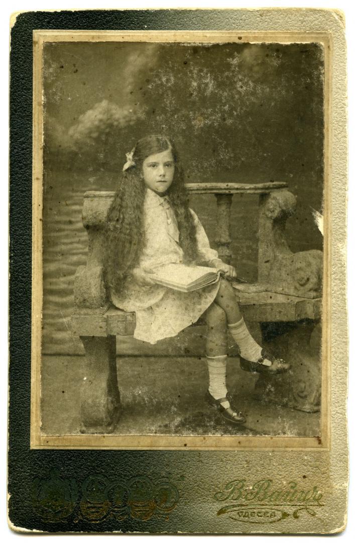 Photo. A little girl holding a book wearing a light dress. 