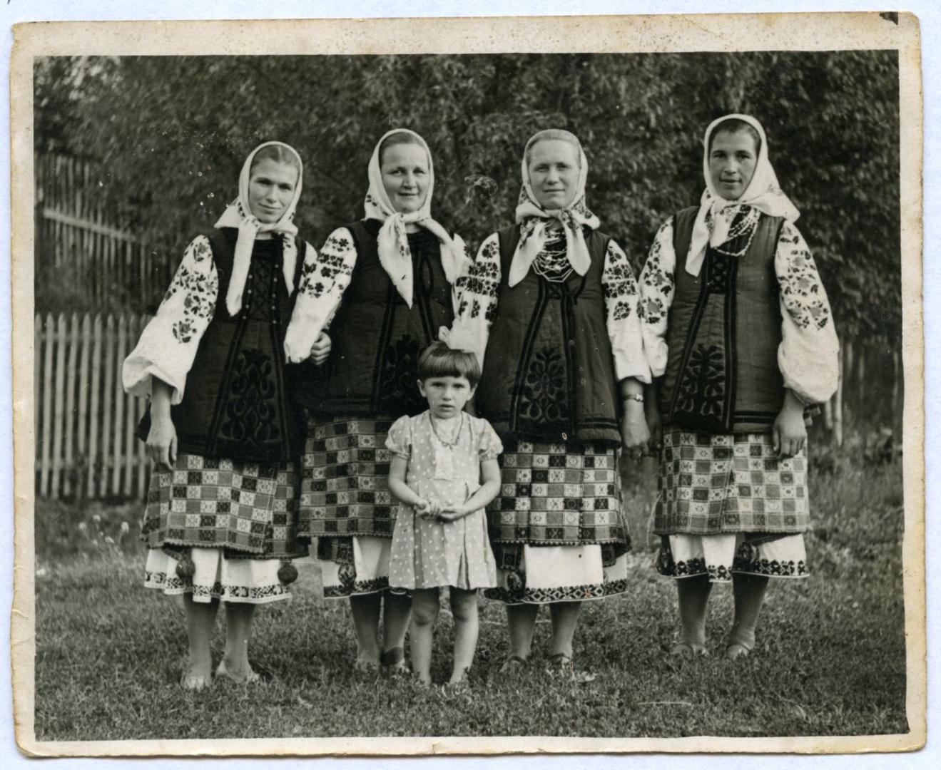 Photo. Women wearing a folk attire in front of an orchard