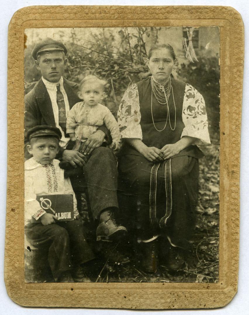 Photo. A man, a young woman, and two children wearing folk attire in front of a house