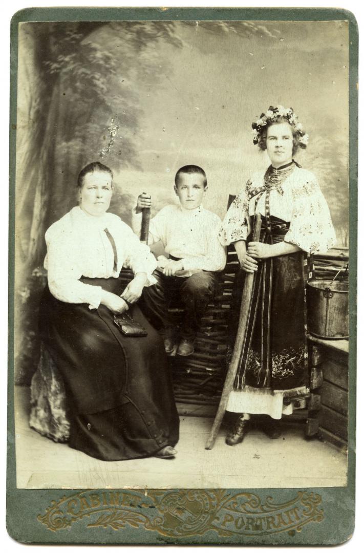 Photo. An older woman, a boy holding a book, a girl with a carrying pole, and a girl wearing stylised Ukrainian attire